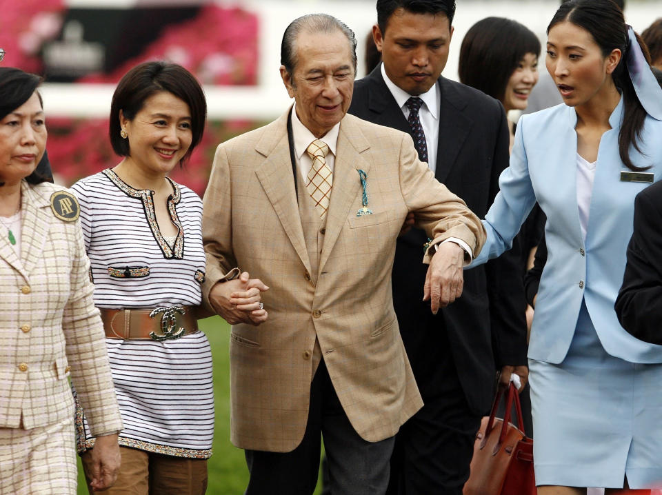 FILE - In this April 29, 2007, file photo, Macao tycoon and owner of Hong Kong horse Viva Pataca Stanley Ho, center, gets a little help from his wife Angela Leung, second left, and an attendant during awarding ceremony at the Sha Tin racecourse in Hong Kong. On Tuesday, May 26, 2020, the family of Stanley Ho, the Macao casino tycoon considered the father of modern gambling in China, has died at 98. (AP Photo/Vincent Yu, File)