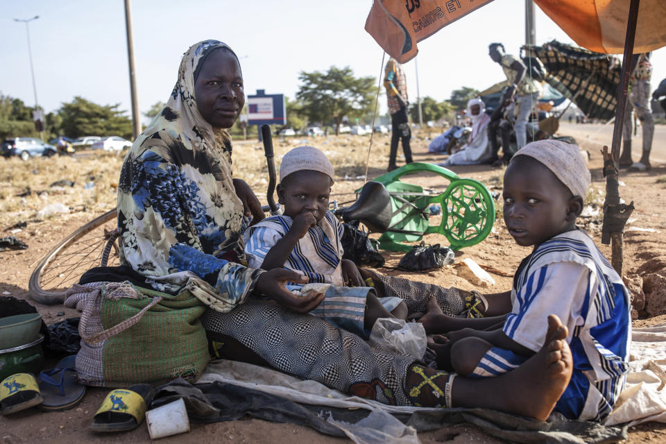 A woman and her twins sit together Thursday, Nov. 25, 2021 at the Patte d'Oie district in Ouagadougou, Burkina Faso, where mothers of twins come to beg on the road. In Burkina Faso, a country with a strong belief in the supernatural, twins are regarded as children of spirits whose mothers were specially selected to bear them. (AP Photo/Sophie Garcia)