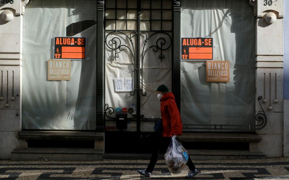 A woman wearing a face-mask walks past a closed store in Lisbon, Portugal on 25 November 2021 - Pedro Nunes/Reuters