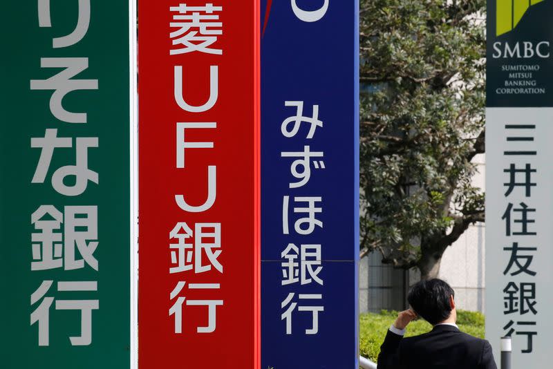 A man walks past signboards of Sumitomo Mitsui Banking Corporation, Mizuho Bank, MUFG Bank, and Resona Bank in Tokyo