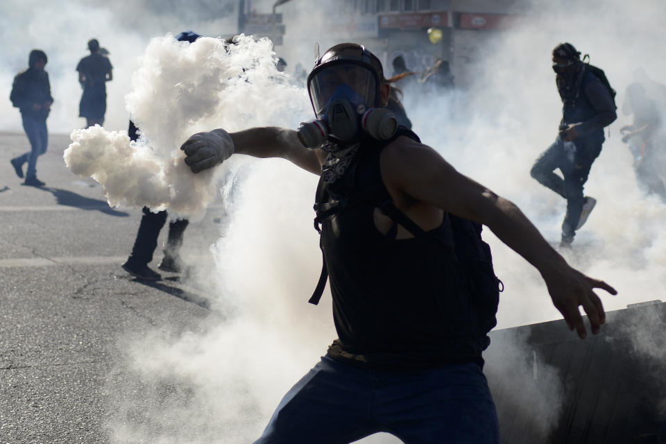 An anti-government protester returns a tear gas canister to police during clashes in Valparaiso, Chile, Friday, Oct. 25, 2019. A new round of clashes broke out Friday as demonstrators returned to the streets, dissatisfied with economic concessions announced by the government in a bid to curb a week of deadly violence.(AP Photo/Matias Delacroix)