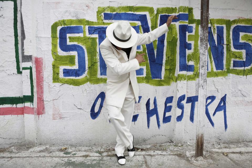 Macias Sotelo wears his "Pachuco" outfit while posing for a photograph next to a wall with graffiti in Mexico City