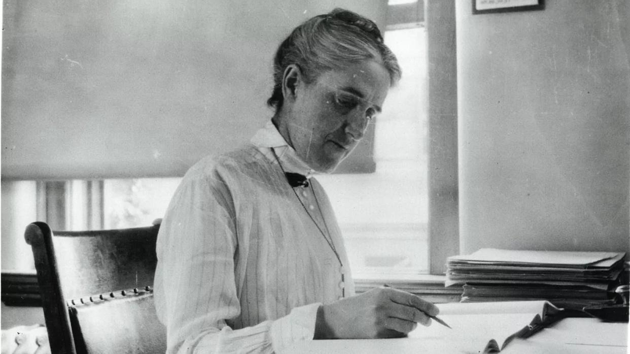  black-and-white photo of a woman sitting at a desk making calculations with a pencil 