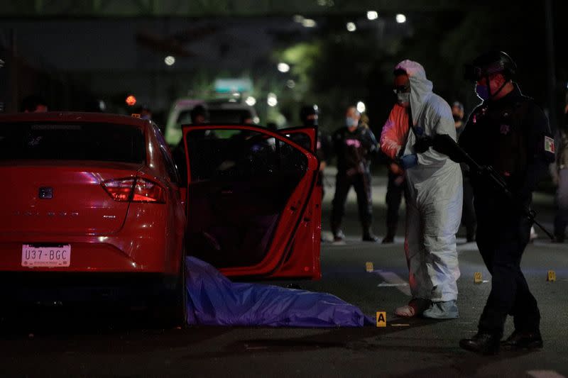 A forensic technician and a police officer stand by the body of a man at a crime scene where unknown assailants attacked a vehicle, in Ecatepec de Morelos
