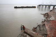 A woman washes her clothes near a damaged jetty in the aftermath of Cyclone Amphan, at Sagar Island