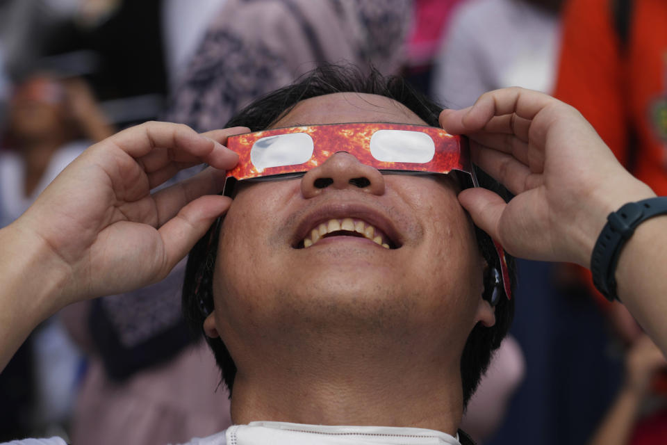 A man, looking excited, uses cardboard eye protection to look up at the sun.