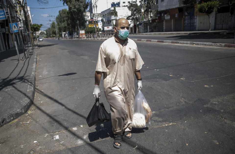 A Palestinian man wears a face mask and gloves carries his shopping during a lockdown imposed following the discovery of coronavirus cases in the Gaza Strip, Thursday, Aug. 27, 2020. On Wednesday Gaza's Hamas rulers extended a full lockdown in the Palestinian enclave for three more days as coronavirus cases climbed after the detection this week of the first community transmissions of the virus in the densely populated, blockaded territory. (AP Photo/Khalil Hamra)