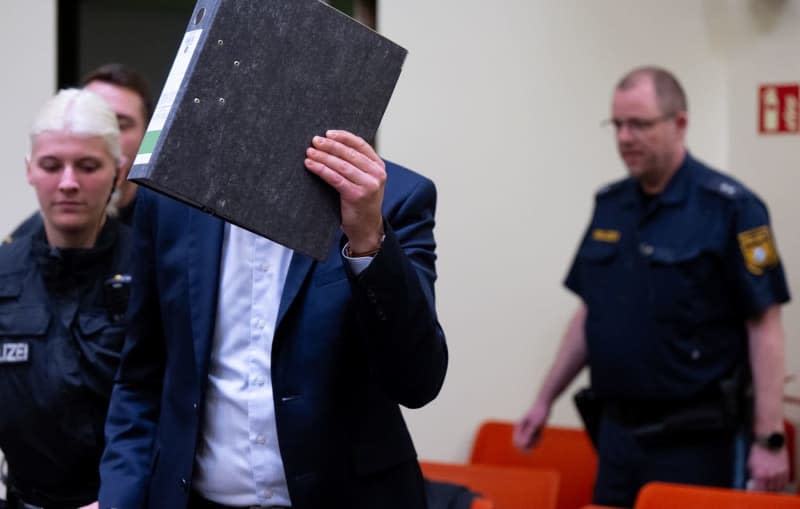 A man accused of belonging to a terrorist organization and planning a so-called high treasonous operation is led into the courtroom at the Higher Regional Court. The Munich Higher Regional Court (OLG) will hold the third countrywide trial against the group's suspected 