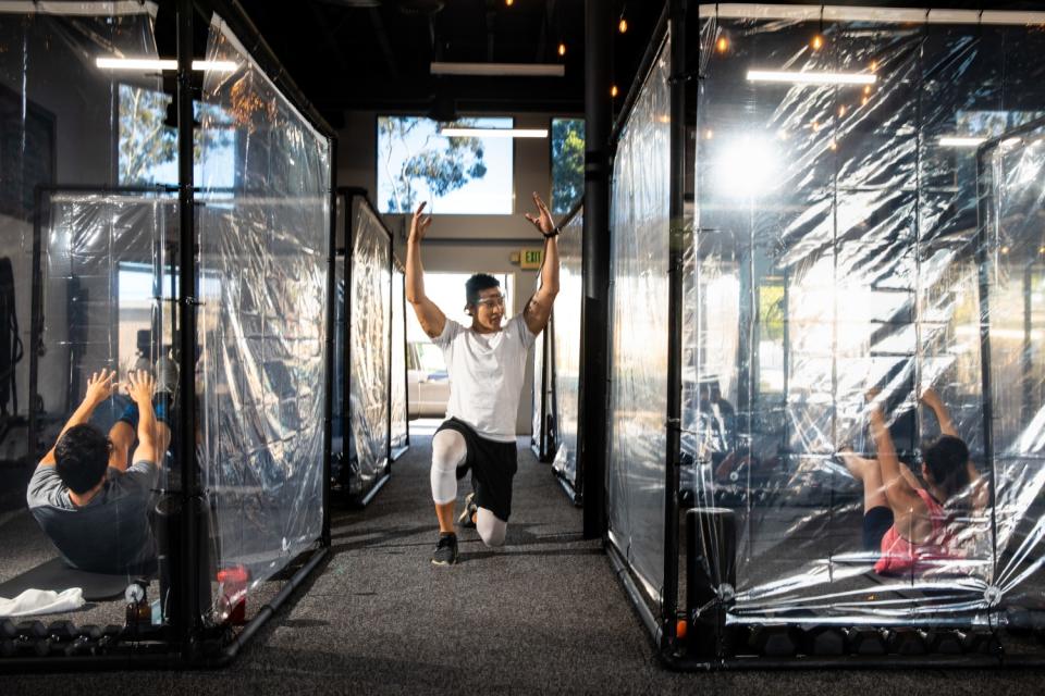 People do sit-ups inside plastic-sided cubicles as a trainer kneels between the cubicles.