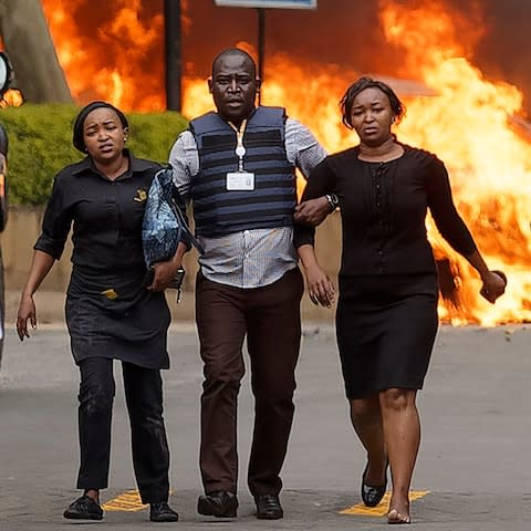 Security forces help civilians flee the scene as cars burn behind - Credit: &nbsp;Ben Curtis/&nbsp;AP