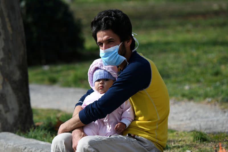 A man holding a baby wears a protective face mask as he sits outside the AHEPA hospital, where the first confirmed coronavirus case is being treated, in Thessaloniki