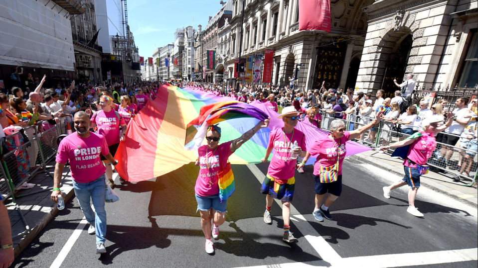 Participants wearing pink t-shirts and carrying a giant rainbow flag walk down the street as people on the pavement cheer
