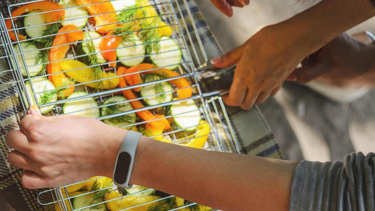 Woman are fill grill lattice with slices of zucchini, pepper and dill before roasting.