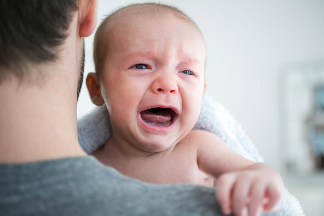 An image of a baby crying over their dad's shoulders.