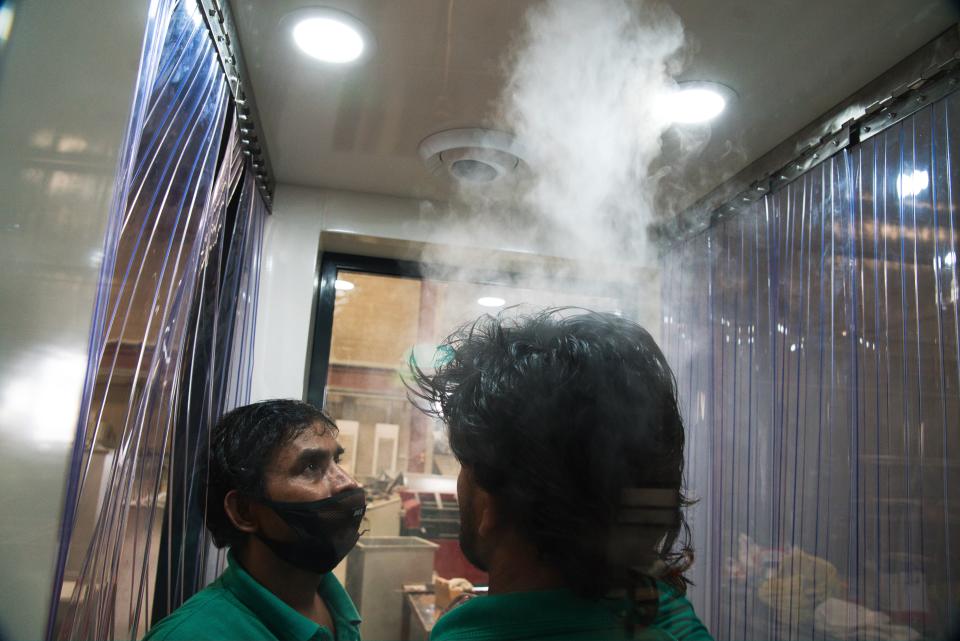 In this Monday, April 27, 2020 photo, workers examine a gate system made by Guard ME that conducts temperature checks and fogs disinfectants on users, in Dubai, United Arab Emirates. As confirmed coronavirus cases spike, the United Arab Emirates is opening up its cavernous malls and restaurants in a gamble to stimulate its economy while still trying to fight off the pandemic. That's led to a new normal here of temperature checks, social distancing monitors at supermarkets and marked-off empty seats on the city's driverless Metro. (AP Photo/Jon Gambrell)