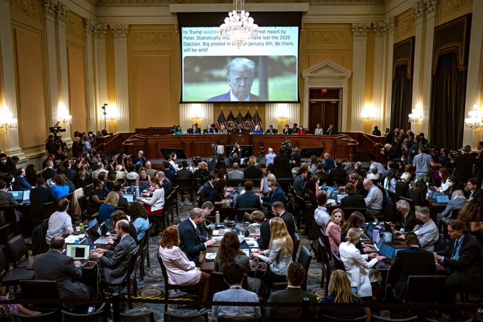 Trump appears on a screen as people watch during a hearing.