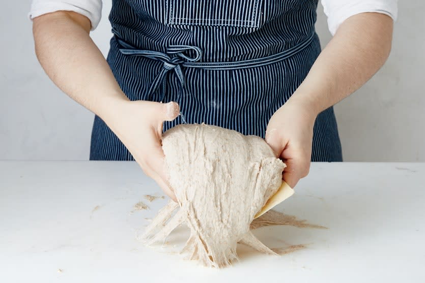 Use a bench scraper in one hand to help move, shape, and scrape the bread dough off your surface. A little bench flour should help, too.