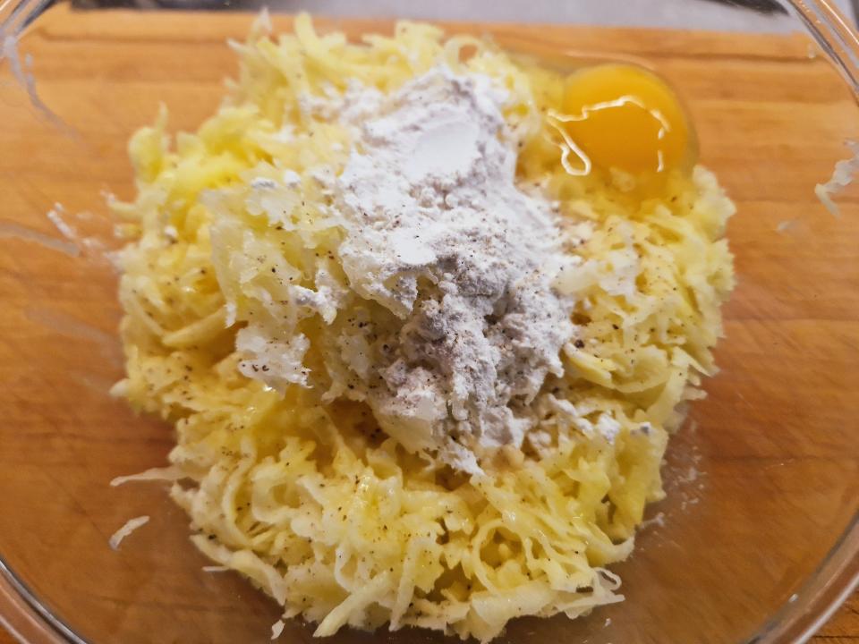 grated potatoes, flour, and an egg in a bowl