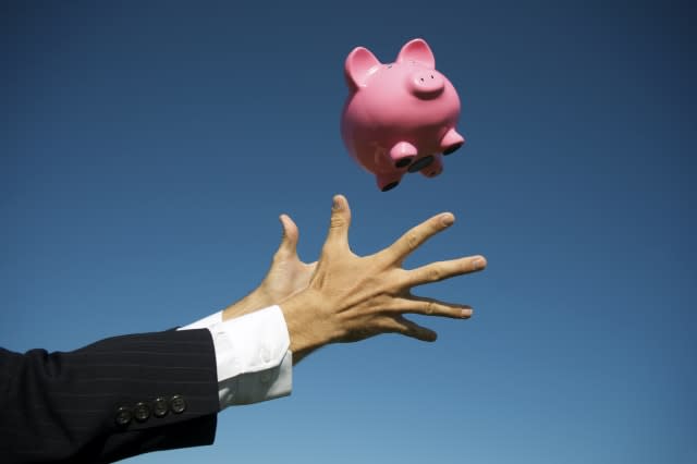 Pair of male hands in suit and barrel cuffs reaches out to catch pink piggy bank falling in blue sky