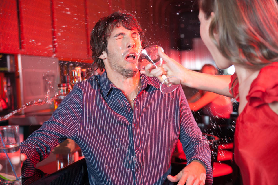 Woman in red top splashing water at man in striped shirt, expressing conflict