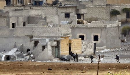 Unidentified armed men run in the Syrian town of Kobani, as seen from near the Mursitpinar border crossing on the Turkish-Syrian border in the southeastern town of Suruc in Sanliurfa province October 15, 2014. REUTERS/Kai Pfaffenbach