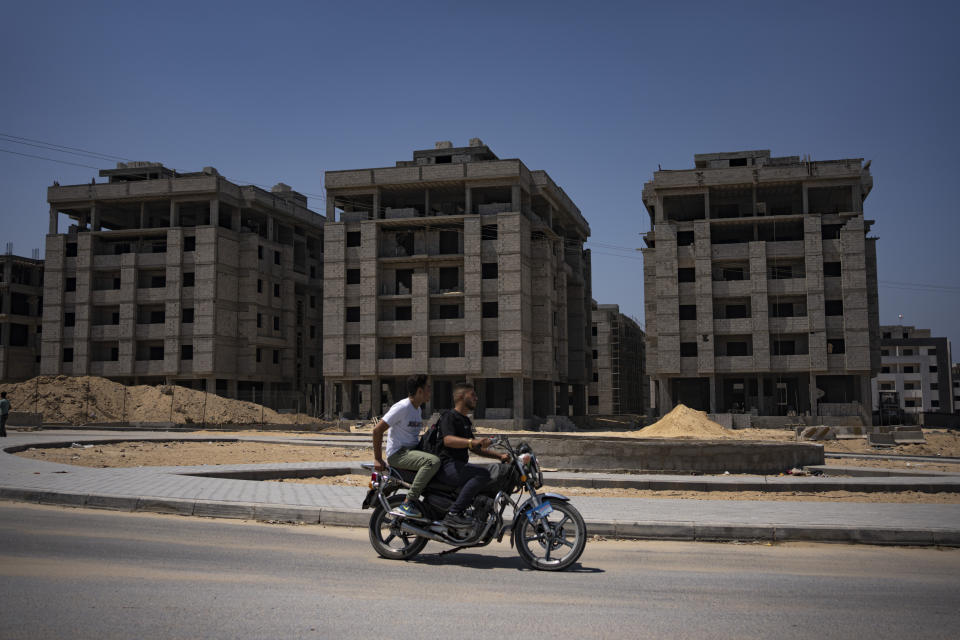 Palestinians on a motorcycle pass nearly completed Egyptian-funded residential buildings in northern Gaza Strip, Sunday, Aug. 27, 2023. Scores of displayed Palestinian families are awaiting completion of nearly 1,400 homes, but the project has become mired in political disputes between the Palestinian Authority and Gaza’s Hamas-run government.(AP Photo/Fatima Shbair)