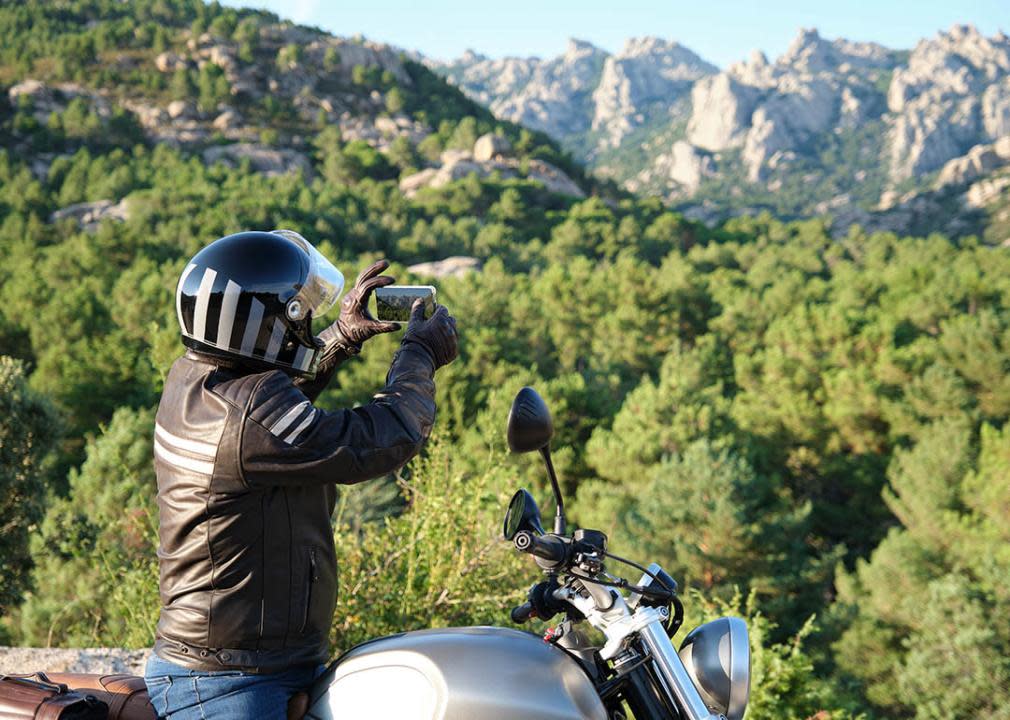 motorcyclist taking photos of scenery by side of the road, mountains and greenery