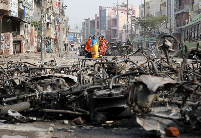 Women walk past charred vehicles in a riot affected area following clashes between people demonstrating for and against a new citizenship law in New Delhi