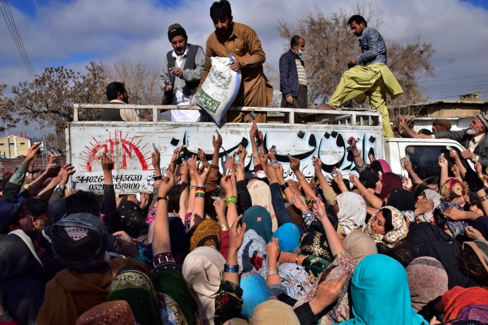 People jostle each other to buy subsidised sacks of wheat flour in Quetta, Pakistan, amid heatwaves and flood displacement (AP)