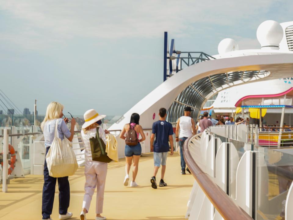 People walk around the top deck of the cruise ship on a sunny day