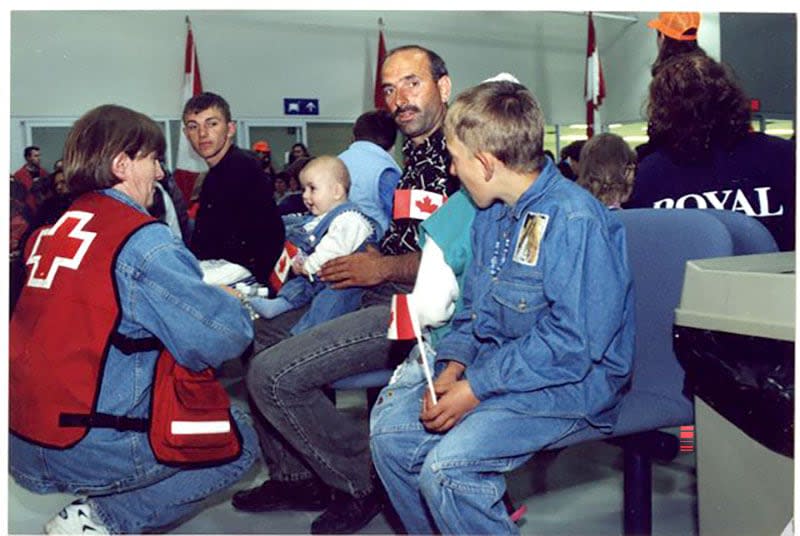 A Red Cross volunteer welcomes a recently arrived Kosovar refugee family awaiting immigration and medical screening at CFB Trenton in 1999. (Canadian Museum of Immigration at Pier 21 Collection (D2017.635.61) - image credit)