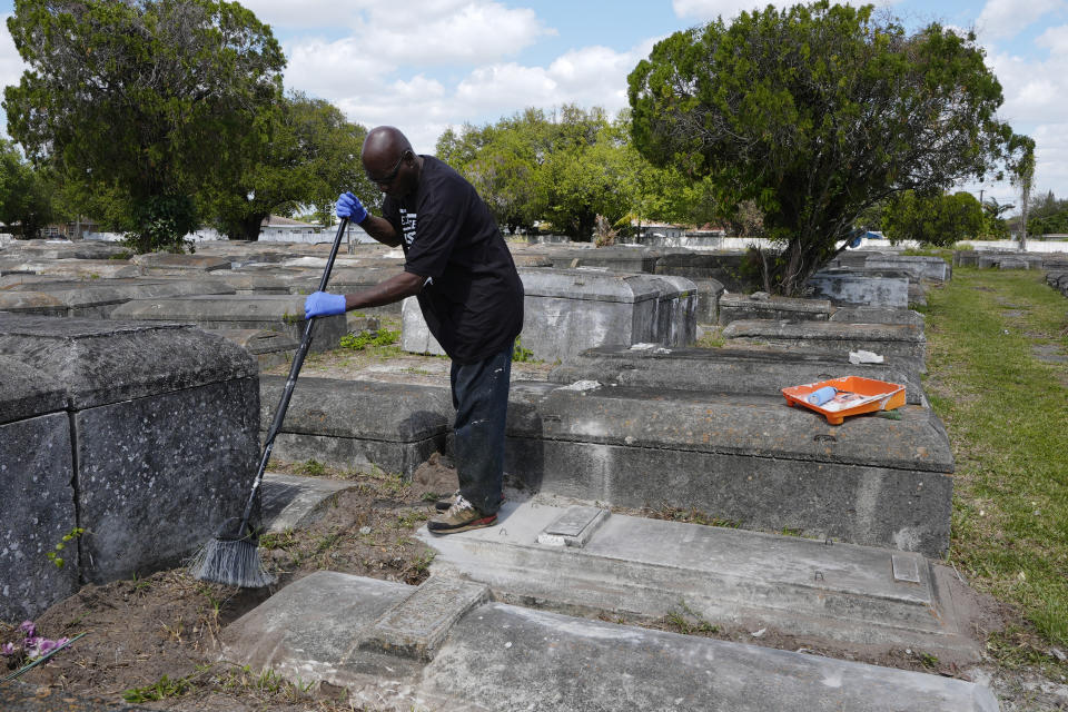 Frank Wooden sweeps the graves of a local family at the Lincoln Memorial Park Cemetery, Monday, Feb. 26, 2024, in the Brownsville neighborhood of Miami. Wooden became the caretaker after his brother, Jessie, purchased the historically segregated Black cemetery where their mother is buried. “When we got here it looked like a jungle,” Frank Wooden said. “Some people had to jump the fence to get in to see their loved one.” (AP Photo/Marta Lavandier)