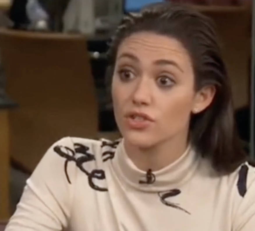 Emmy in a top with dark accents seated speaking during the interview