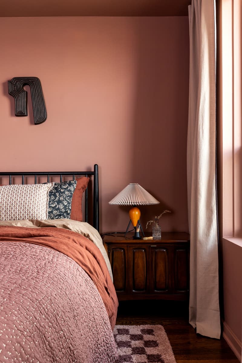 Wood based lamp on nightstand in dusty pink bedroom.