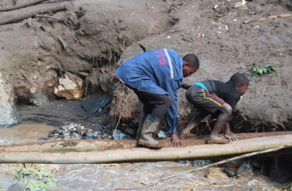 A man and child cross a river on a log filled with mud in Bududa District, Uganda, Friday, Oct. 12, 2018. At least 30 people died in mudslides triggered by torrential rains in a mountainous area of eastern Uganda that is prone to such disasters, a Red Cross official said Friday. More victims were likely to be discovered when rescue teams access all the affected areas in the foothills of Mount Elgon, said Red Cross spokeswoman Irene Nakasiita. (AP Photo/ Ronald Kabuubi)