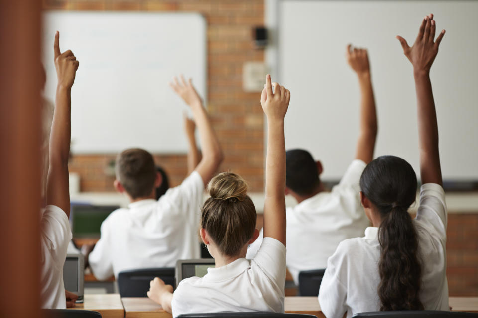 Kids in a classroom raise their hands.