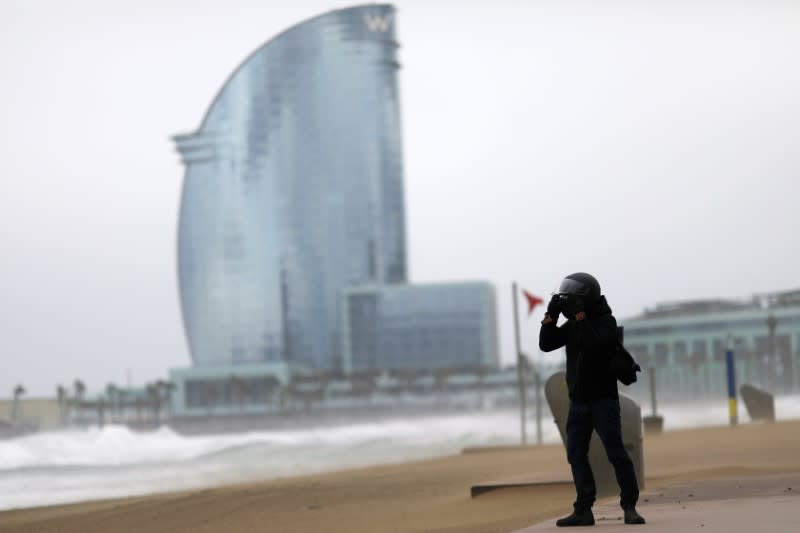 Man uses his motorcycle helmet to protect his face from beach sand, as he takes pictures of the storm "Gloria" in front of Barceloneta Beach, in Barcelona