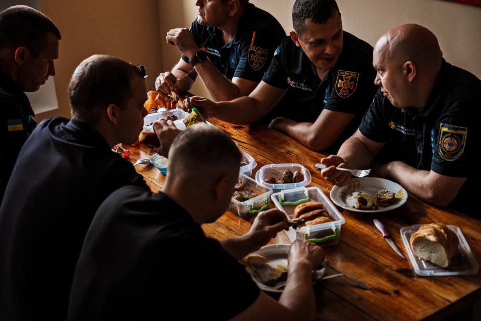 Six firefighters sit around a table eating