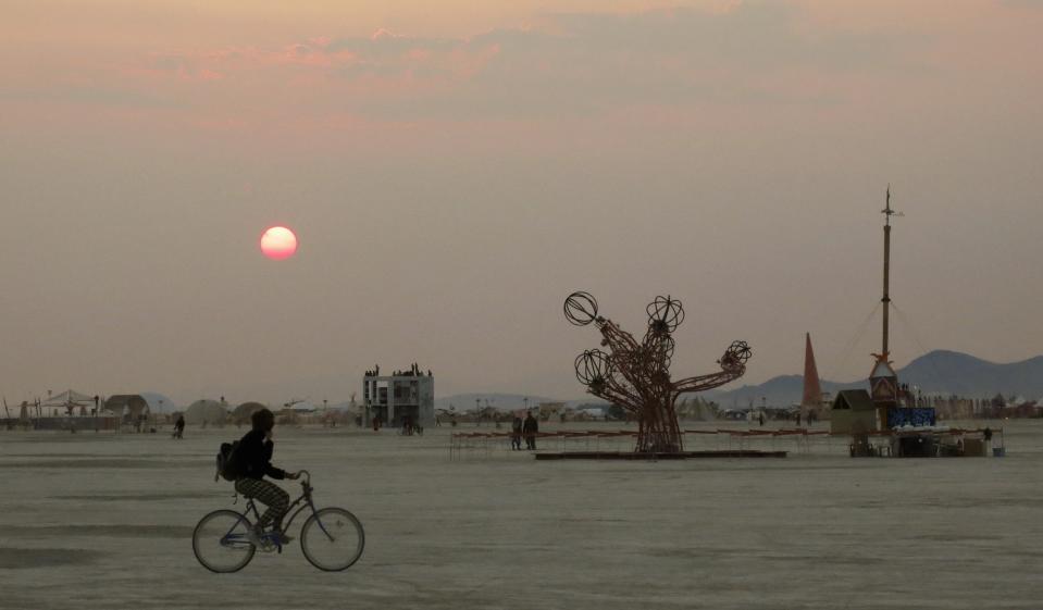 A participant bicycles past art works on the playa at sunrise, during the 2013 Burning Man arts and music festival in the Black Rock desert of Nevada