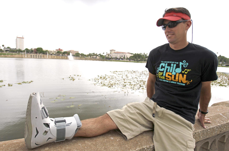 In this photo taken Thursday, April 19, 2012, Greg Farris takes a break while wearing a protective boot as he helps set up for a weekend triathlon event in Lakeland, Fla. Farris injured his foot while running in barefoot running shoes.(AP Photo/John Raoux)