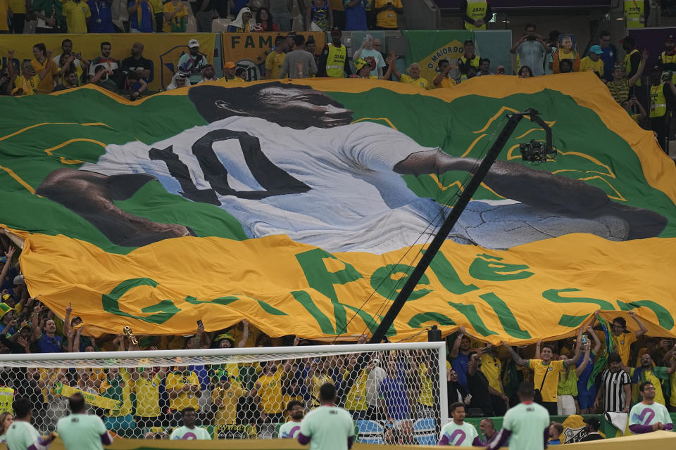 Soccer fans hold a giant Brazilian flag with a picture of Brazilian soccer legend Pele with a message reading in English "Pele, Get well soon," during the World Cup group G soccer match between Cameroon and Brazil, at the Lusail Stadium in Lusail, Qatar, Friday, Dec. 2, 2022. (AP Photo/Pavel Golovkin)