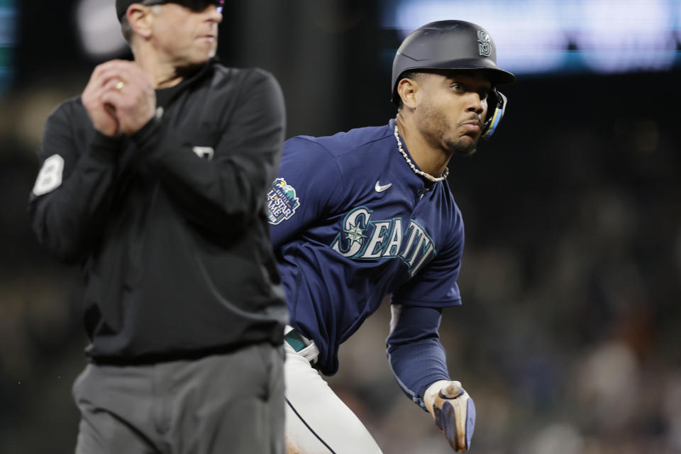 FILE - Seattle Mariners' Julio Rodriguez and umpire Chris Guccione watch the flight of a errent throw as Rodriquez goes on to score against the Houston Astros in the fifth inning of a baseball game, Tuesday, Sept. 26, 2023, in Seattle. Seattle center fielder Julio Rodriquez will receive the largest amount in the $50 million pool for pre-arbitration players, earning $1,865,349, according to figures compiled by Major League Baseball and the players’ association. (AP Photo/John Froschauer, File)