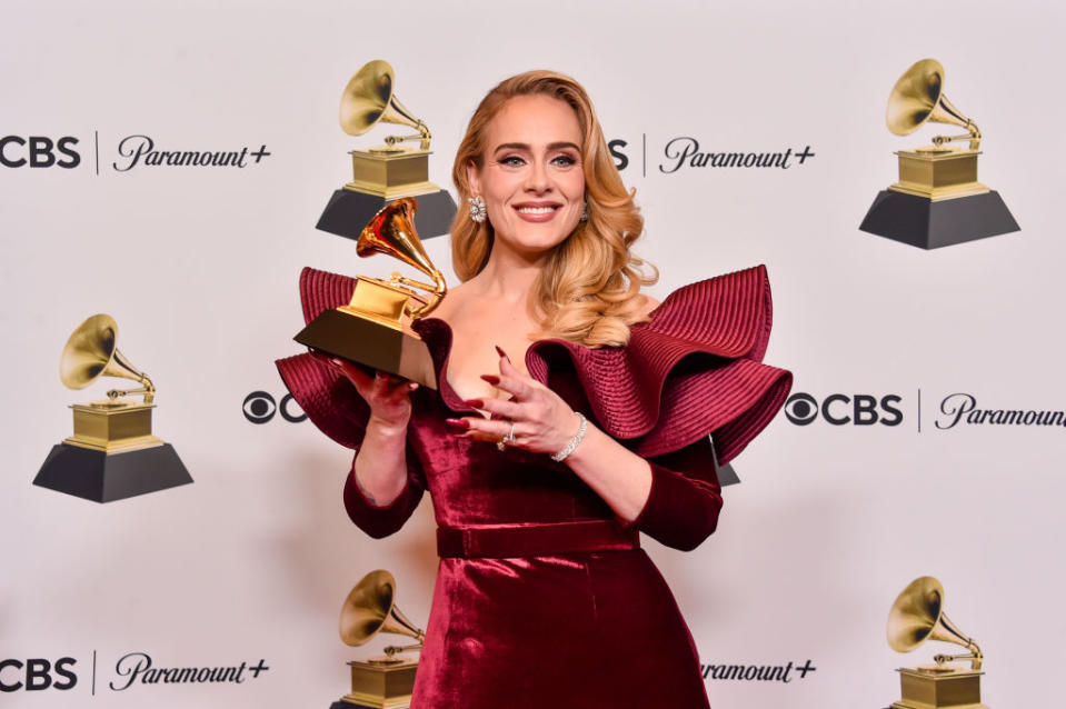 Adele poses with her Grammy award in an elegant off-the-shoulder dress with ruffled sleeves at a CBS and Paramount+ event