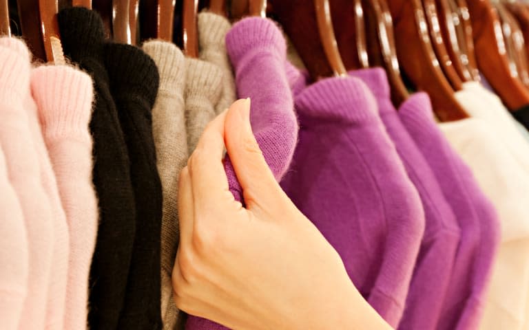 Hand touching cashmere sweater on clothing rack