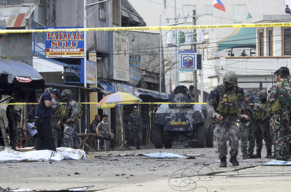 FILE - In this Jan. 27, 2019, file photo, police investigators and soldiers attend the scene after two bombs exploded outside a Roman Catholic cathedral in Jolo, the capital of Sulu province in southern Philippines. Abu Sayyaf commander Hatib Hajan Sawadjaan accused of plotting the attack in the cathedral may be harboring a foreign would-be suicide bomber in his jungle base, a senior official said Thursday, Feb. 7, 2019. Sawadjaan's goal was to assert his new role as Islamic State group leader in the southern Philippines. (AP Photo/Nickee Butlangan, File)
