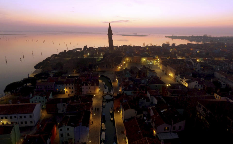 This image taken on Thursday, Jan. 16, 2020, shows an overview of the Burano island at sunset, Italy. The Venetian island of Burano's legacy as a fishing village remains the source of its charms: the small colorful fishermen's cottages, traditional butter cookies that were the fishermen's sustenance at sea and delicate lace still stitched by women in their homes. As the island's population dwindles, echoing that of Venice itself, so too are the numbers of skilled artisans and tradespeople who have kept the traditions and economy alive. (AP Photo/Luca Bruno)