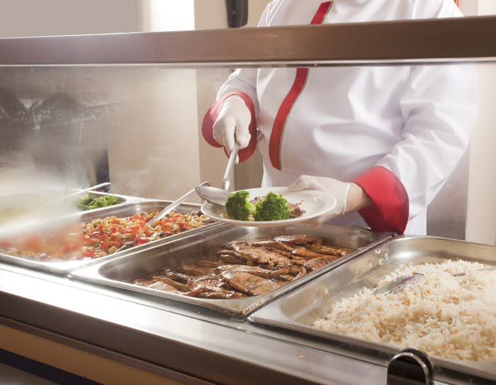 A cafeteria worker serving food from a steam table