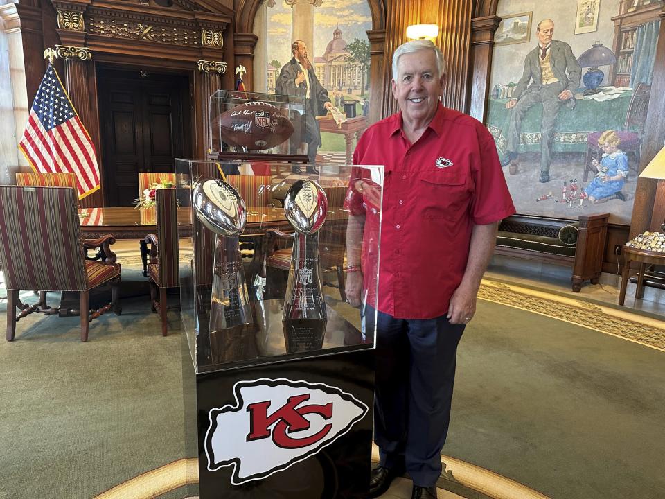 Missouri Gov. Mike Parson poses next to the Kansas City Chiefs' two most recent Super Bowl trophies on display in his Capitol office in Jefferson City, Mo., Thursday, June 27, 2024. Parson said Missouri is working on a public aid proposal for new or improved stadiums for Chiefs and Kansas City Royals. (AP Photo/David A. Lieb)