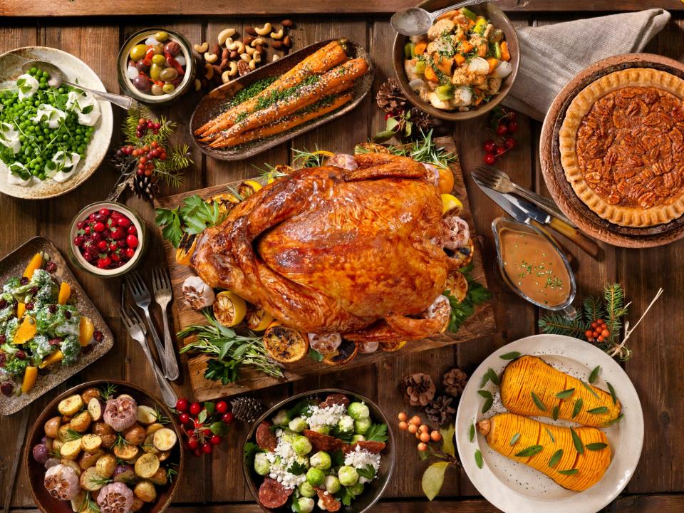 A table loaded with a Thanksgiving feast, including turkey, gravy, cranberries, carrots, peas, potatoes, squash, salad, and pecan pie.