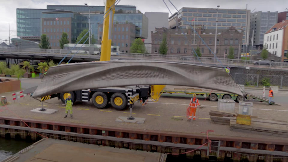Construction workers using a crane to hoist a 3D-printed bridge in Amsterdam.